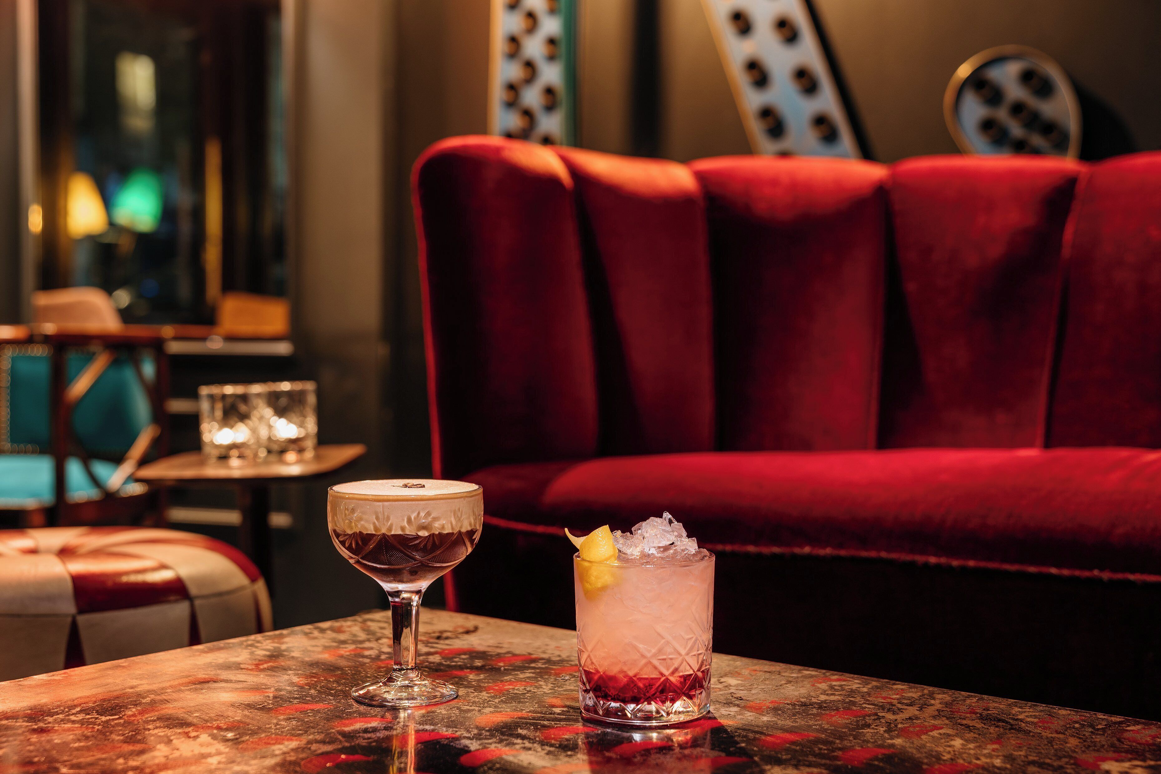 A bar area with a red upholstered sofa, a table with two drinks, and a glass with a lemon slice.