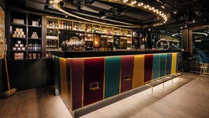 A bar with a colorful, striped counter and shelves of bottles. - Ruby Lucy Hotel London by IHG (London)