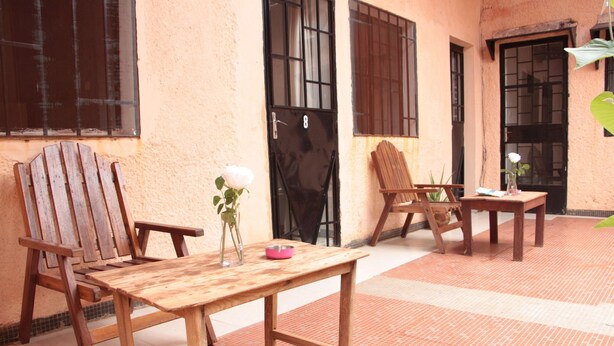 A wooden table and chairs set on a tiled floor with a window and door in the background. - Ouaka Hotel (Ouagadougou)