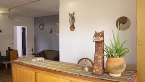 A reception area with a wooden counter, a potted plant, and decorative wall art including a zebra head and a cat sculpture. - Ouaka Hotel (Ouagadougou)