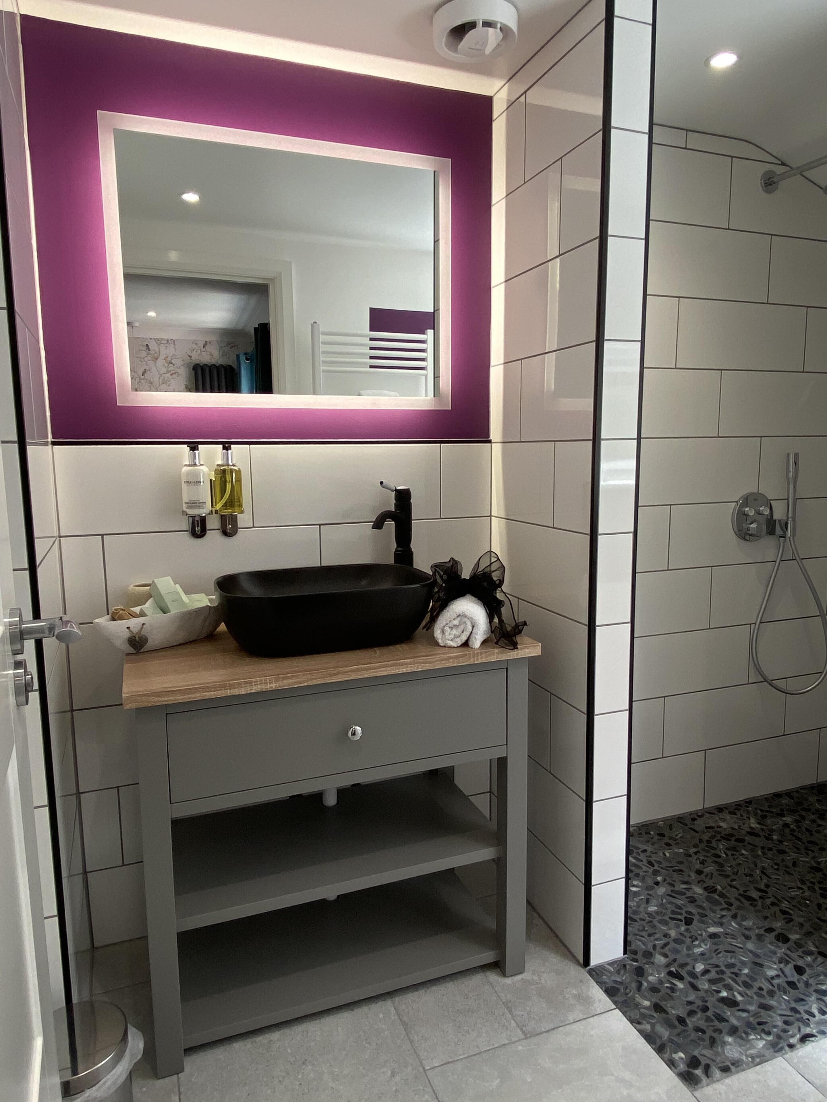 A modern bathroom with a black basin, a mirror, and a shower.