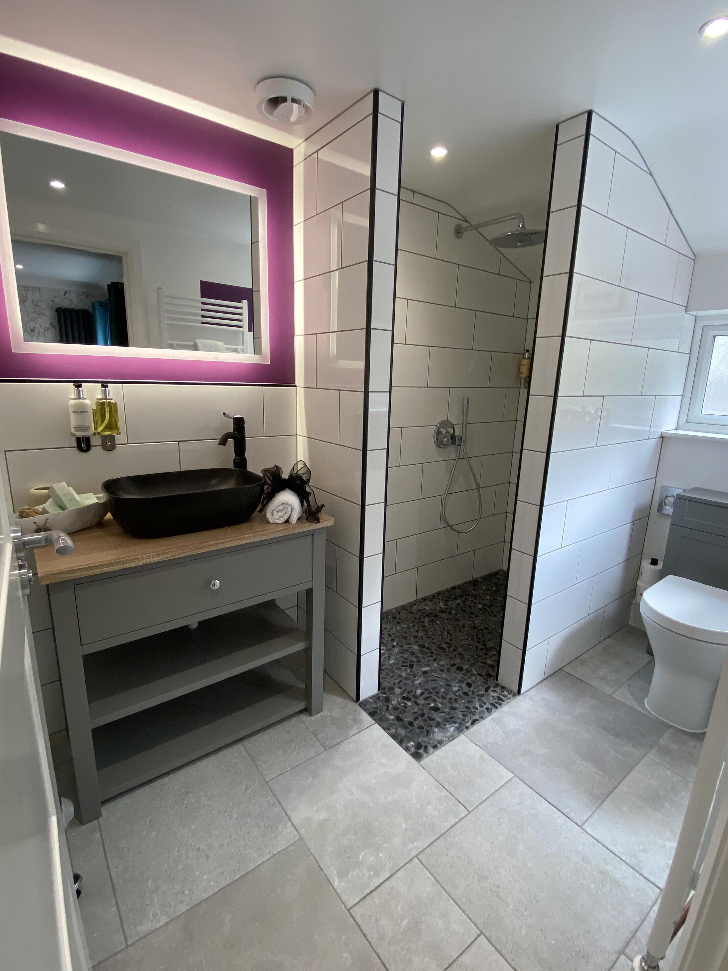 A modern bathroom with a black sink, a mirror with a purple frame, and a shower area.