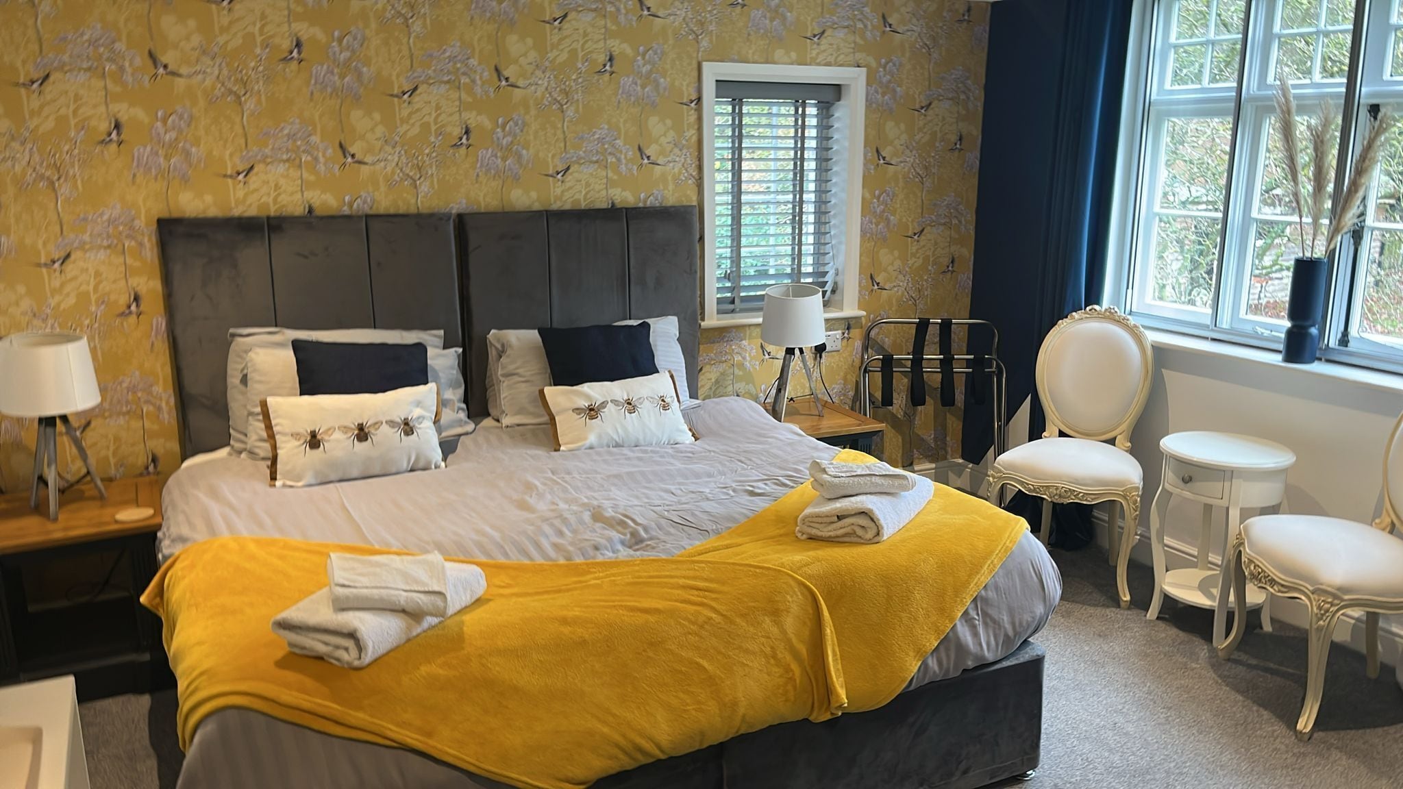 A hotel room with a large bed, two bedside tables, a chair, a small table, and a window with curtains.