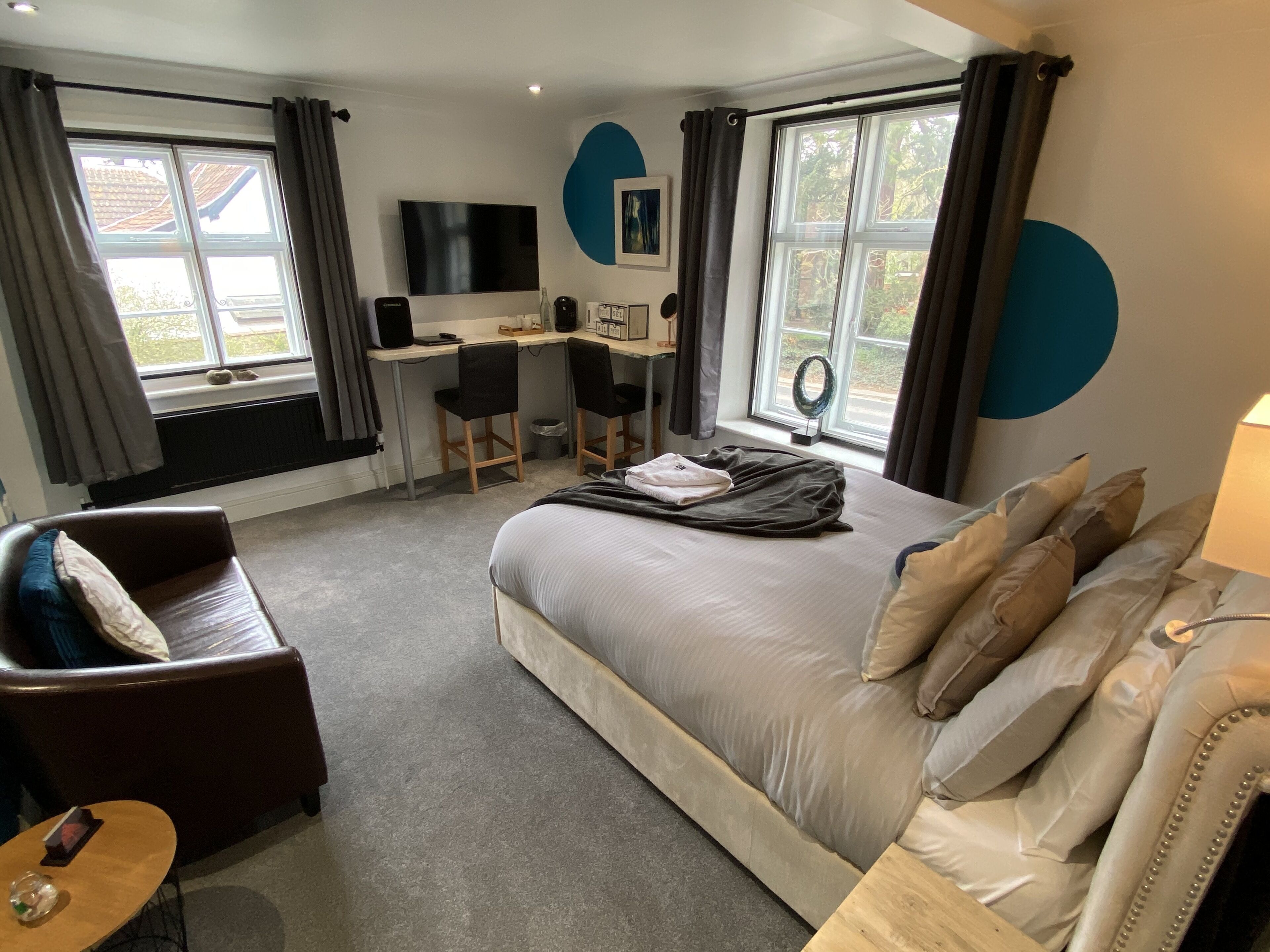 A modern hotel room with a large bed, a desk with two chairs, a television, and a view of the outdoors.
