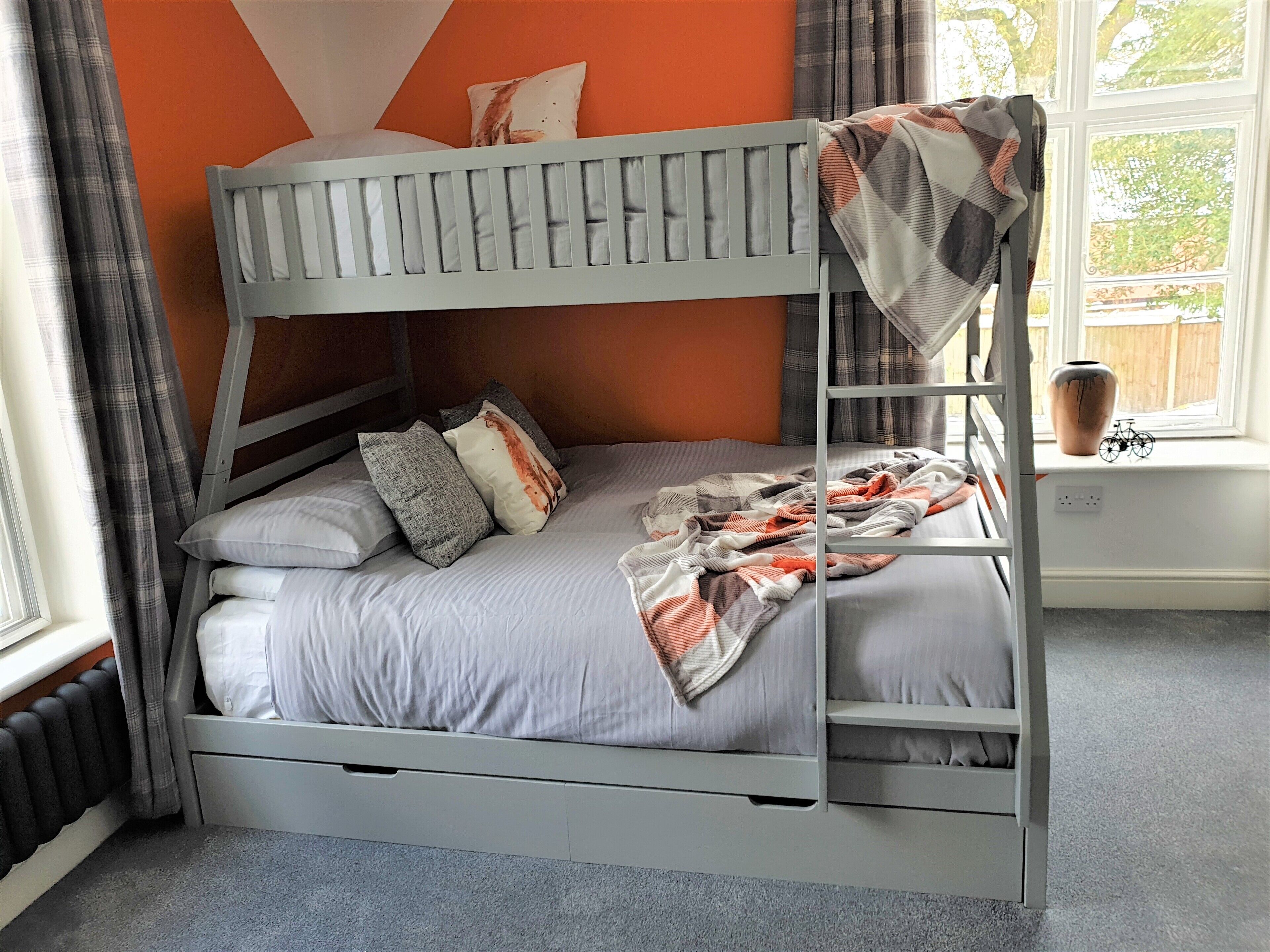 A bunk bed with a grey frame, white bedding, and a patterned blanket.