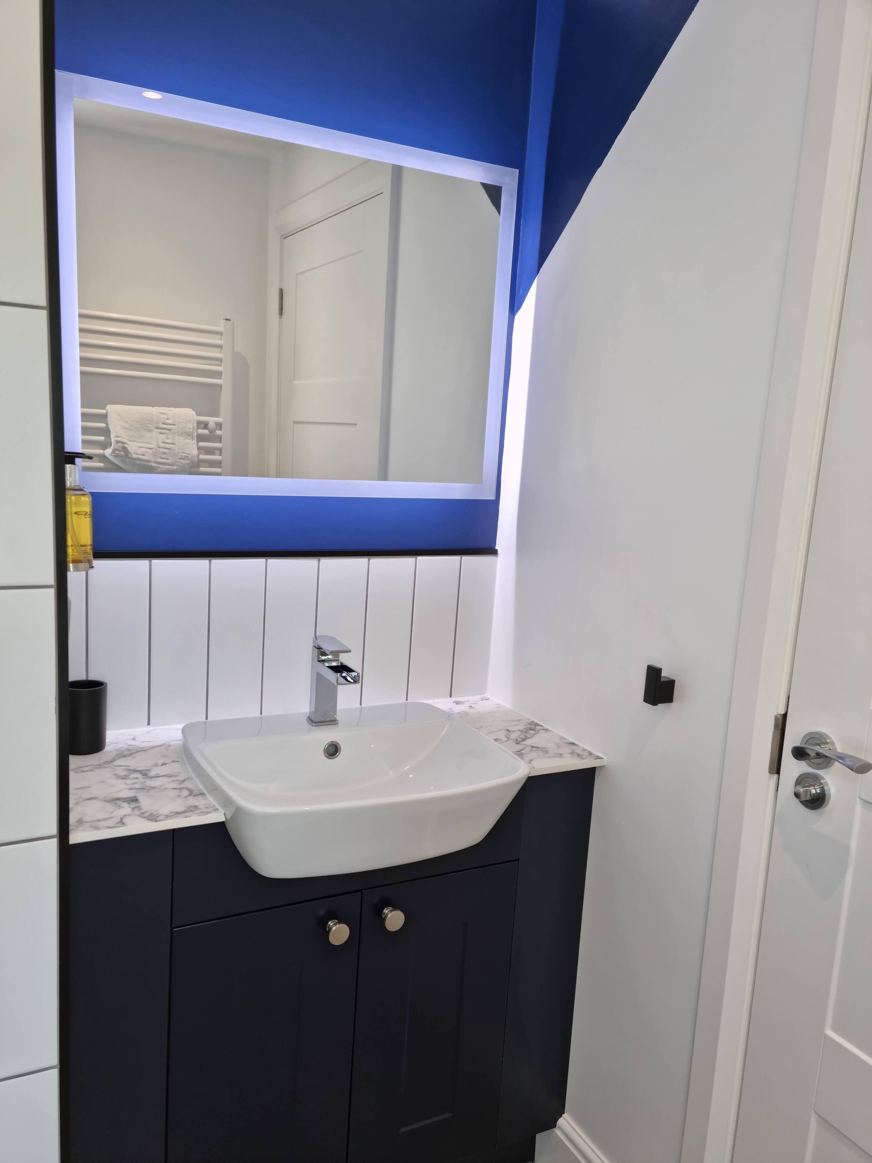 Un baño moderno con un lavamanos blanco, armarios oscuros y una pared azul de acento.