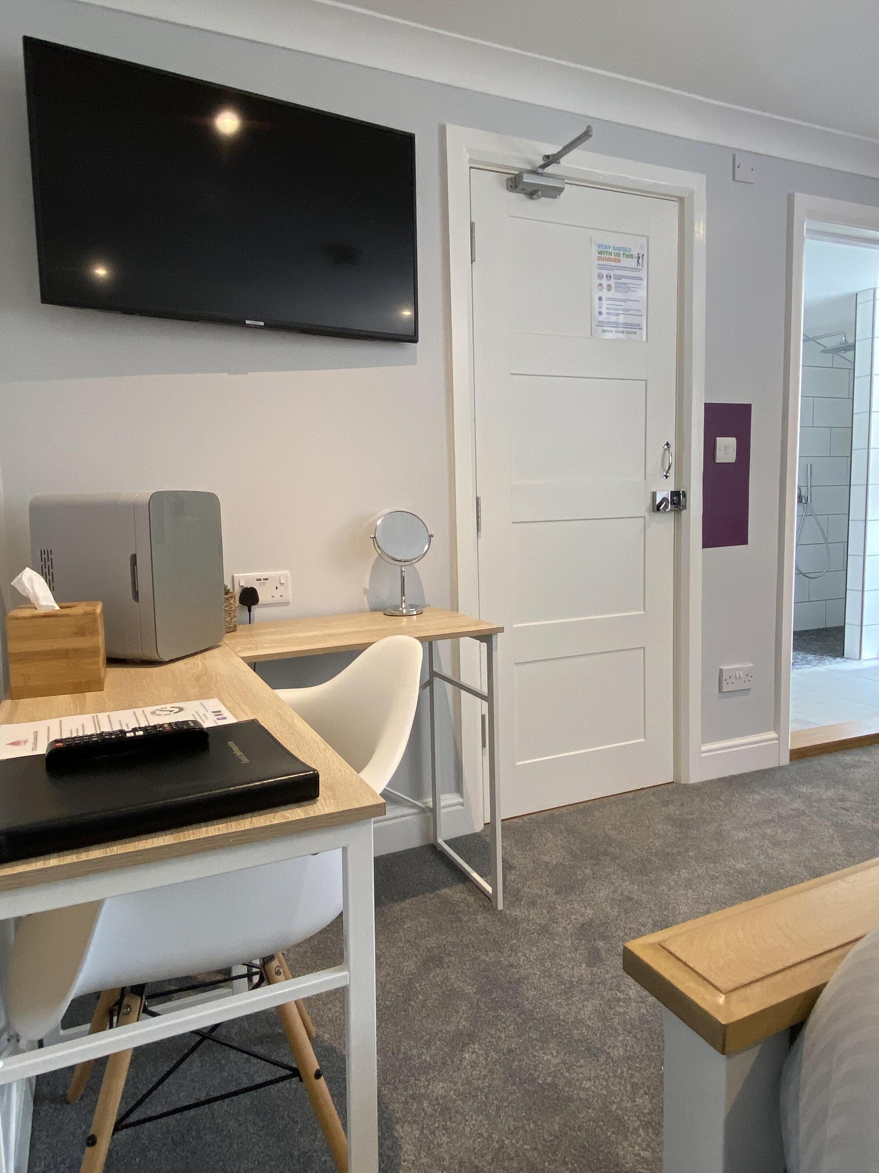 A room with a TV mounted on the wall, a desk with a computer, a chair, and a bed.