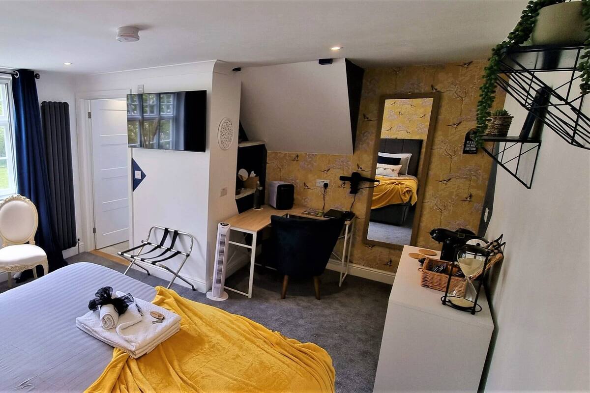 Ett hotellrum med en säng, ett skrivbord, en stol, ett litet bord och ett fönster med gardiner.