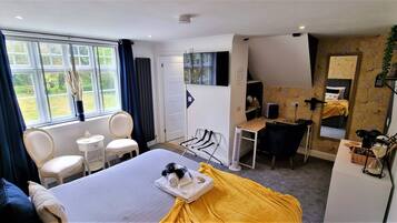 A hotel room with a bed, a desk, a chair, a small table, and a window with curtains.
