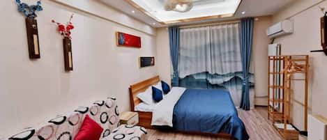 A hotel room with a bed, a sofa, a small table, and a window with curtains.