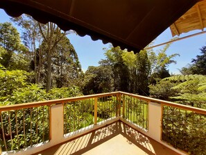 Un balcon en bois offrant une vue sur un jardin luxuriant et de grands arbres.