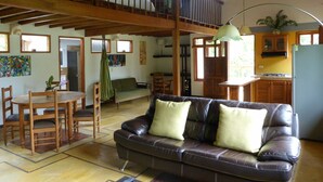 A spacious living area with a leather sofa, wooden dining table, and chairs. A kitchen with wooden cabinets and a refrigerator is visible in the background. - Casa Jade (Rionegro)