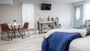 Een slaapkamer met een bed, een bureau, twee stoelen, een televisie en een deur.