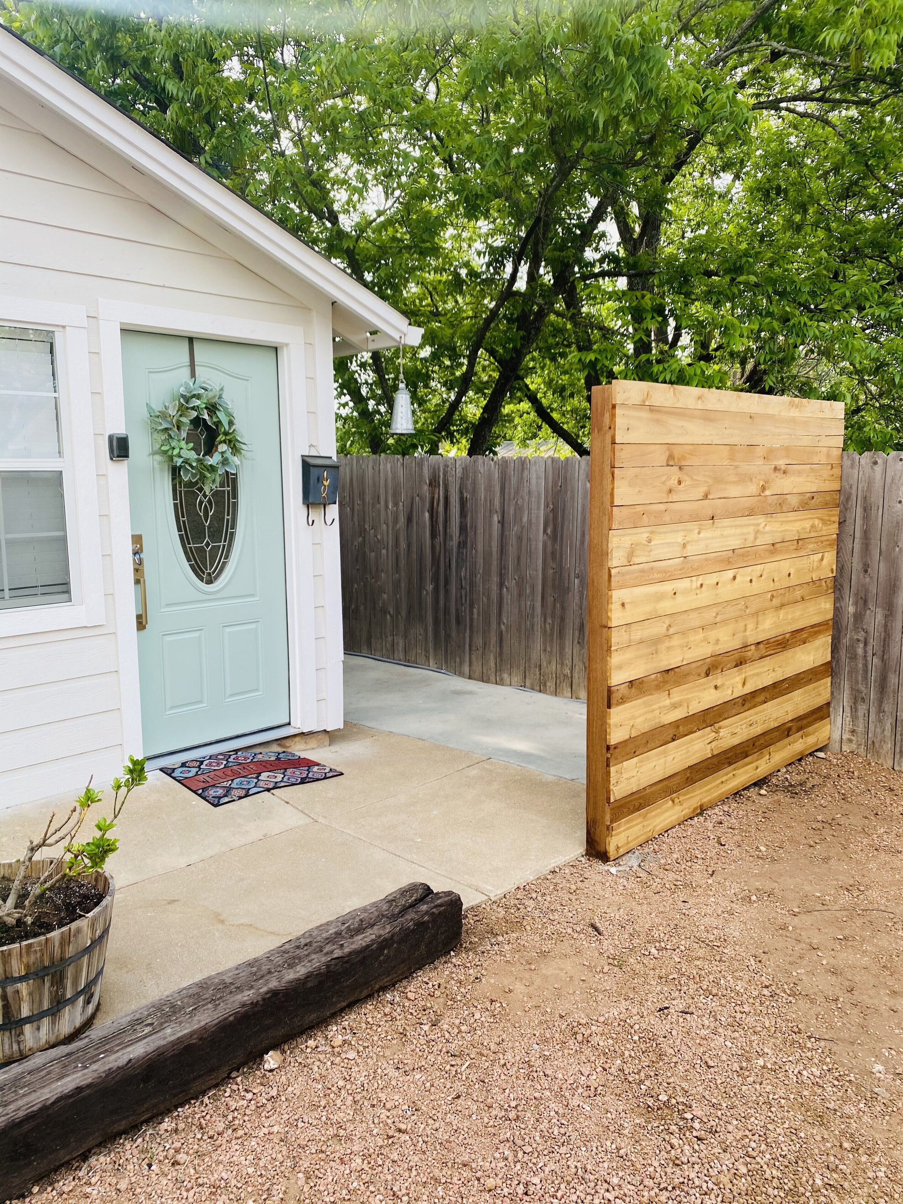 A house with a light blue door, a wooden fence, and a gravel driveway.