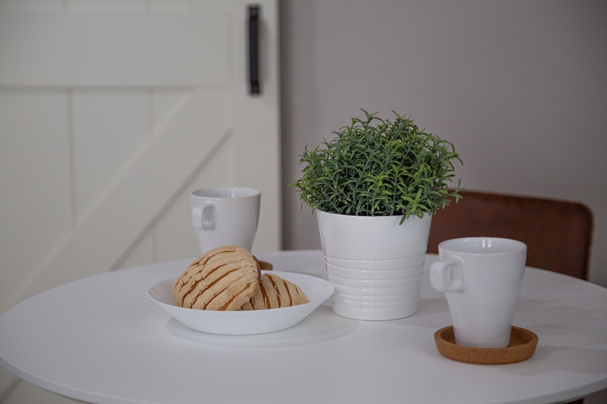 A round white table with a white mug, a plate with cookies, and a white potted plant.