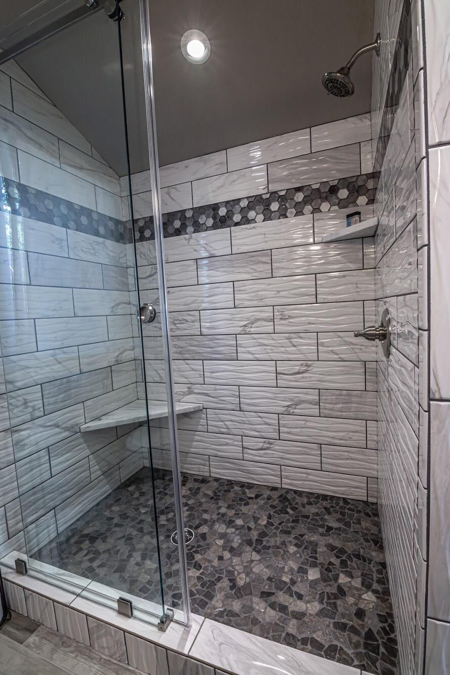 A modern shower with a glass door, tiled walls, and a mosaic floor.