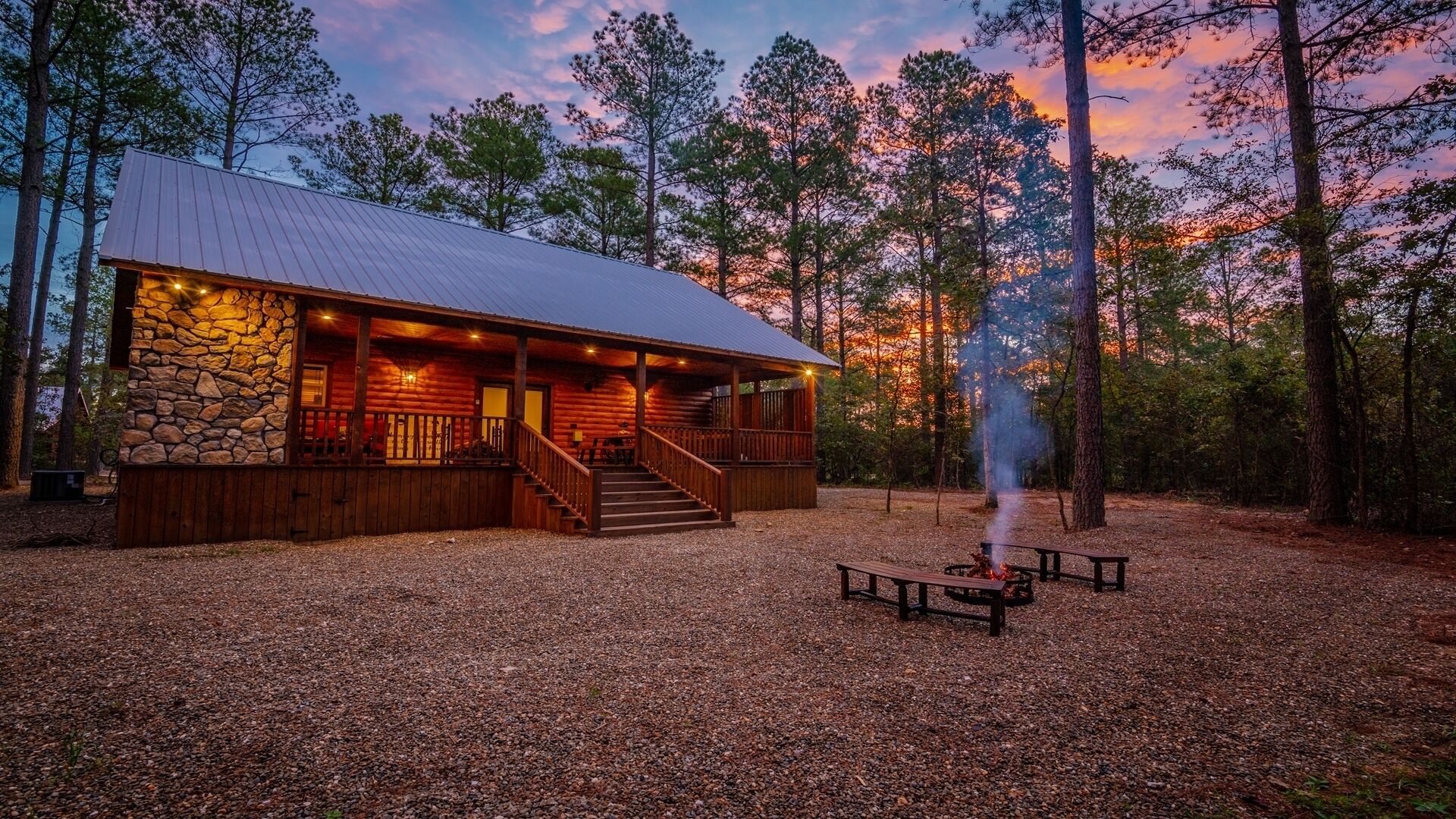 Un chalet rustique avec une façade en pierre, une terrasse en bois et un espace aménagé pour faire un feu de camp.