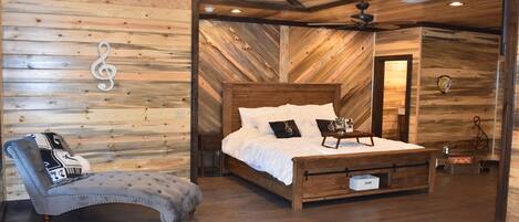 Ein Schlafzimmer mit Holzboden, einem Bett mit weißer Bettwäsche, einem Nachttisch und einem Sessel mit gemustertem Kissen.
