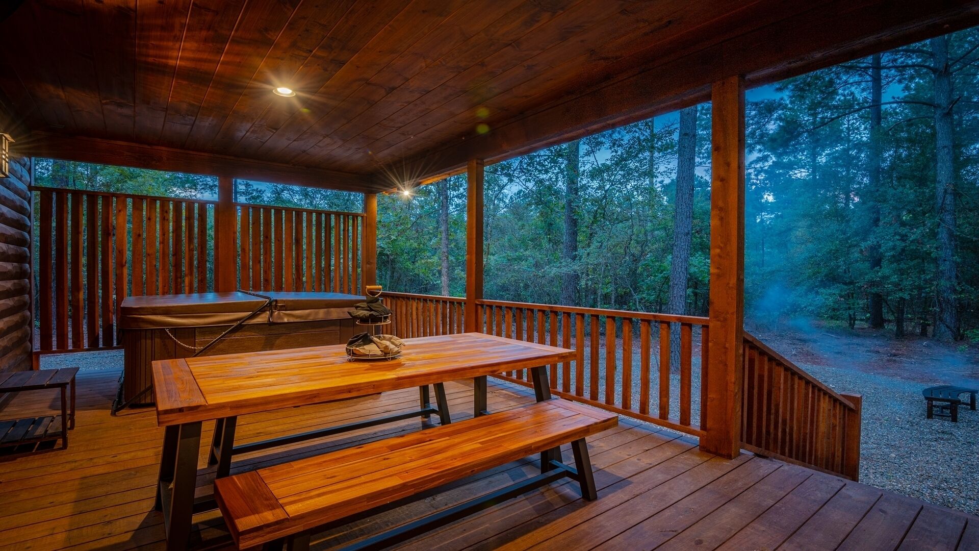 A wooden deck with a picnic table and benches, surrounded by a forested area.
