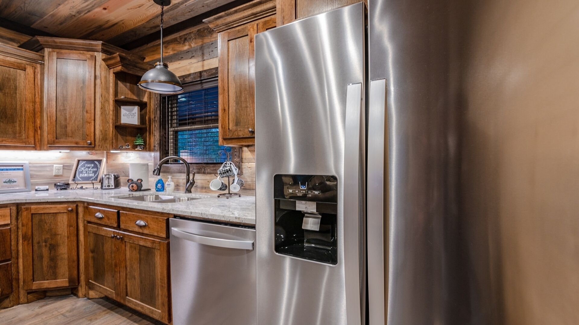 Una cucina con mobili in legno, elettrodomestici in acciaio inossidabile, lavastoviglie integrata e dispenser d'acqua.
