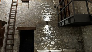 A rustic room with exposed wooden beams, stone walls, a ladder, a sofa, and a hanging light fixture. - Rustic stone house with a modern touch (Civitella Casanova)