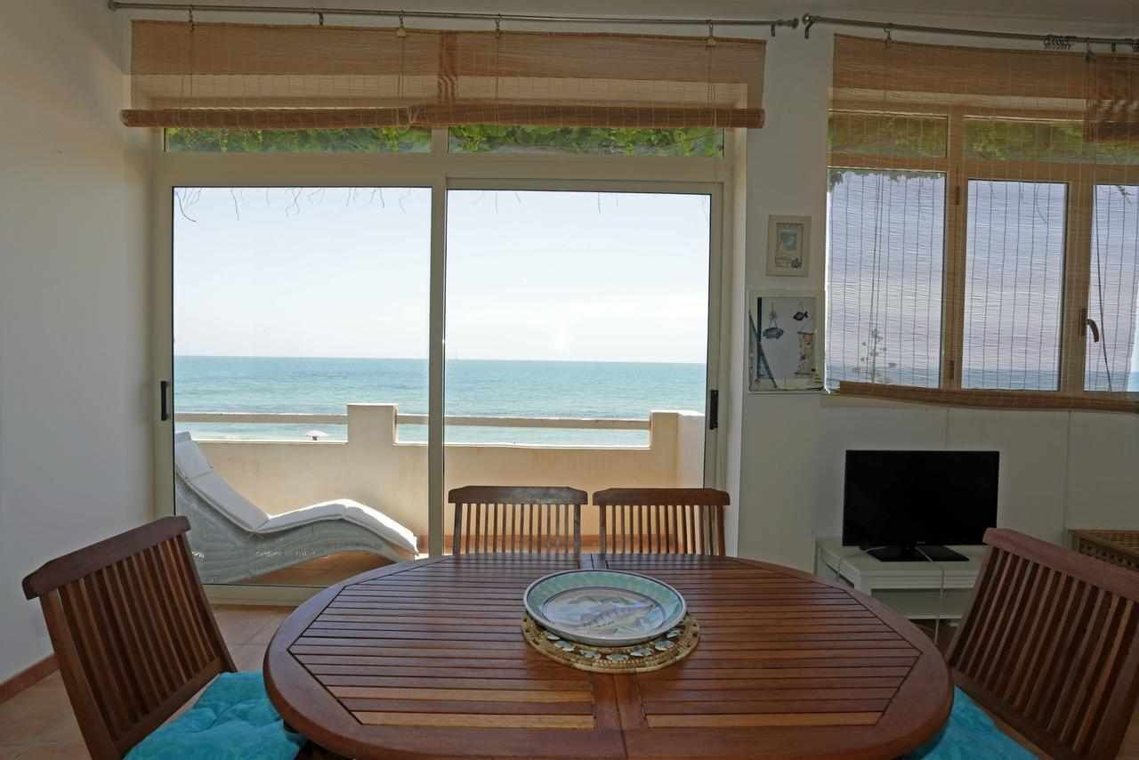 Une pièce avec une table et des chaises en bois, un téléviseur et une vue sur la mer grâce à de grandes fenêtres.