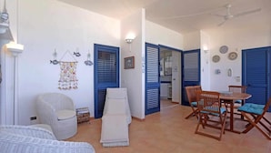 Zona pranzo con tavolo rotondo e sedie, una sedia in vimini e una parete decorata.