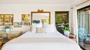 A bedroom with a large bed, a wooden headboard, a mirror, and artwork on the walls. - Poipu Beach Kauai Honeymoon : View Sea Turtles from Your Oceanfront Deck-AC (Koloa)