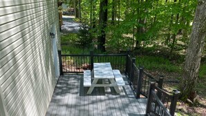 A wooden deck with a picnic table and grill, surrounded by a railing and trees.