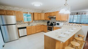 A modern kitchen with wooden cabinets, a stainless steel refrigerator, a microwave, and a large island with stools.
