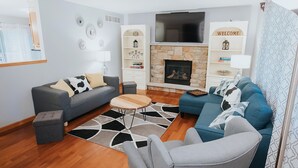 A modern living room with a stone fireplace, grey sofas, and a flat-screen TV.