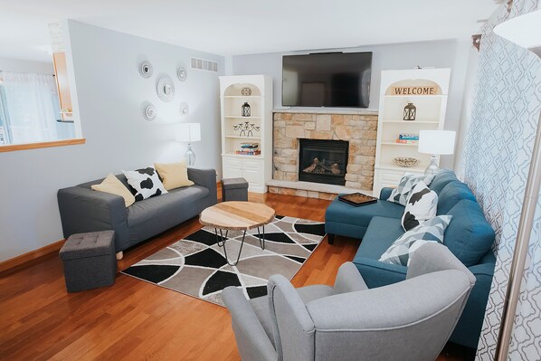 A modern living room with a stone fireplace, grey sofas, and a flat-screen TV.