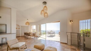 A spacious living area with a wooden table, two ottomans, a sofa, and a kitchen area with a dining set. - Villa 17 - Panoramic view of Palombaggia (Porto-Vecchio)