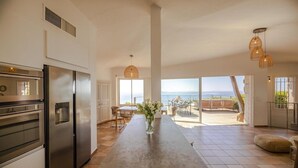 A modern kitchen with a large island, stainless steel appliances, and a view of the sea. - Villa 17 - Panoramic view of Palombaggia (Porto-Vecchio)