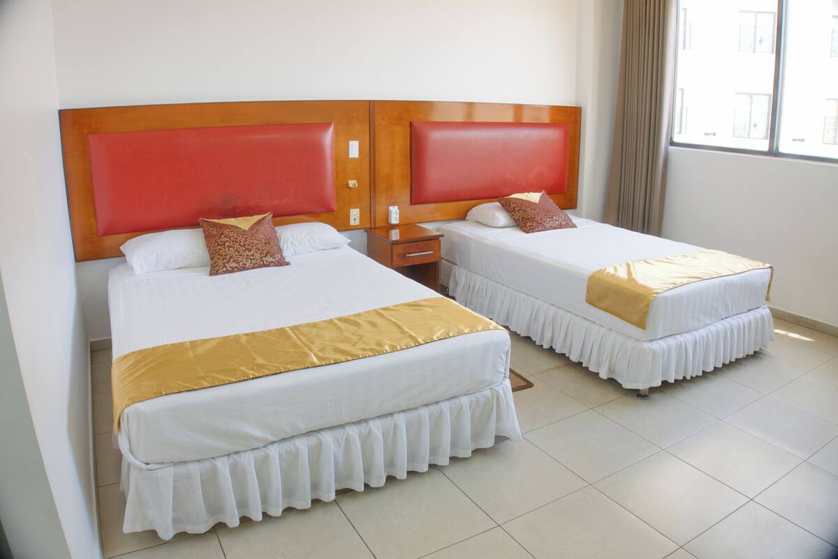 Habitación de hotel con dos camas, cada una con cabecero de madera y ropa blanca.