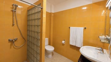 Un baño con baldosas amarillas, cabina de ducha de vidrio, inodoro, lavamanos y un perchero para toallas.