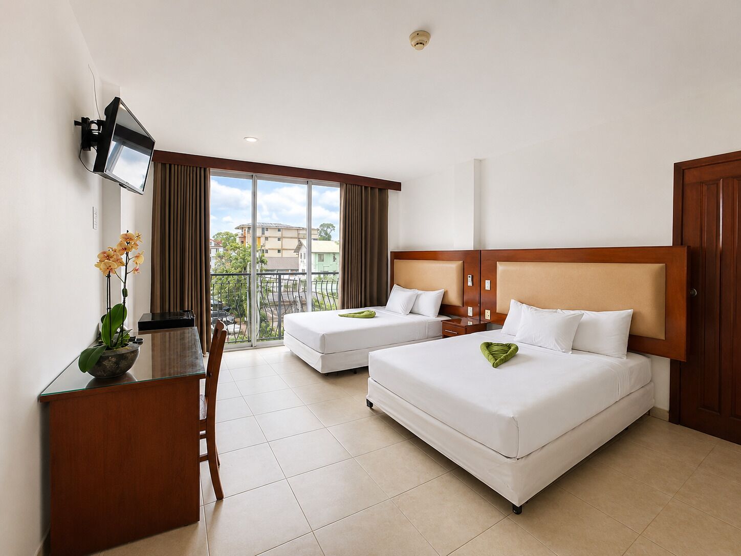 Quarto de hotel com duas camas, uma mesa, televisão e varanda com vista.