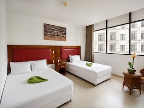 A hotel room with two beds, a painting on the wall, a window with a view of buildings, and a small table with a plant. - Spanhoek Boutique Hotel (Paramaribo)