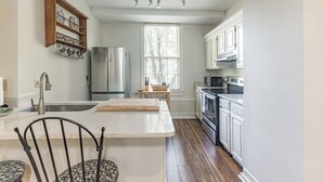 A kitchen with white cabinets, a stainless steel refrigerator, a microwave, and a wooden island with a cutting board. - Historic Cottage with modern amenities (louisville)