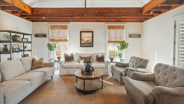 A spacious living room with a high ceiling, wooden beams, a sofa, armchairs, a coffee table, and two side tables. - Historic Cottage with modern amenities (louisville)