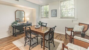 A dining room with a wooden table and chairs, a black console table with a lamp, and two windows with blinds. - Historic Cottage with modern amenities (louisville)