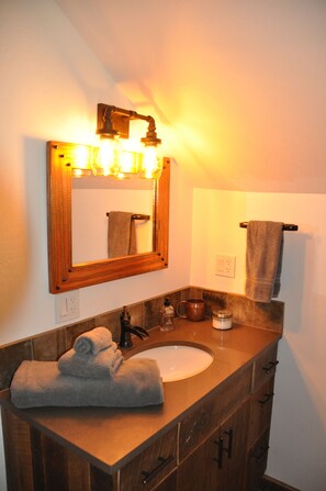 A bathroom with a wooden vanity, a sink, a mirror with lights, and a towel rack. - Lakeside Adventurer's Cabin (Durango)