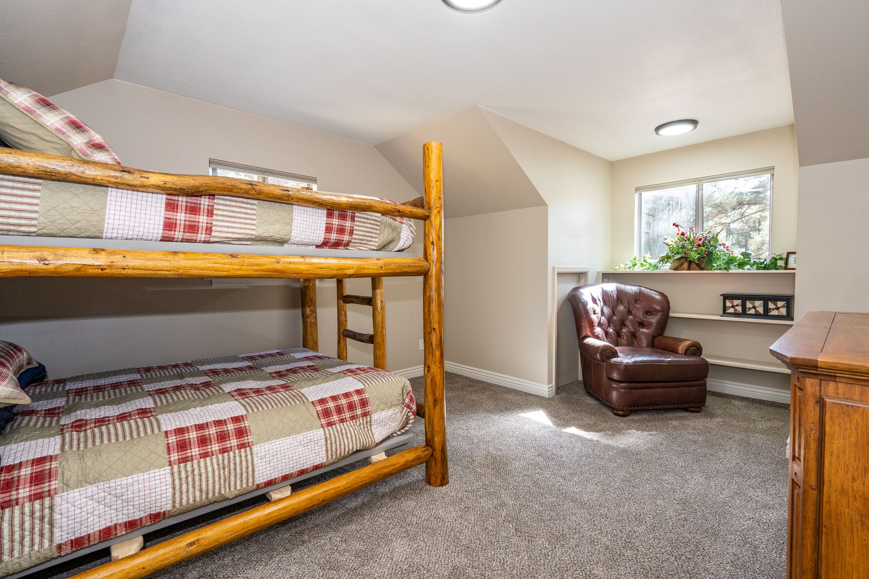 A bunk bed with a quilt, a leather armchair, and a window with a plant.