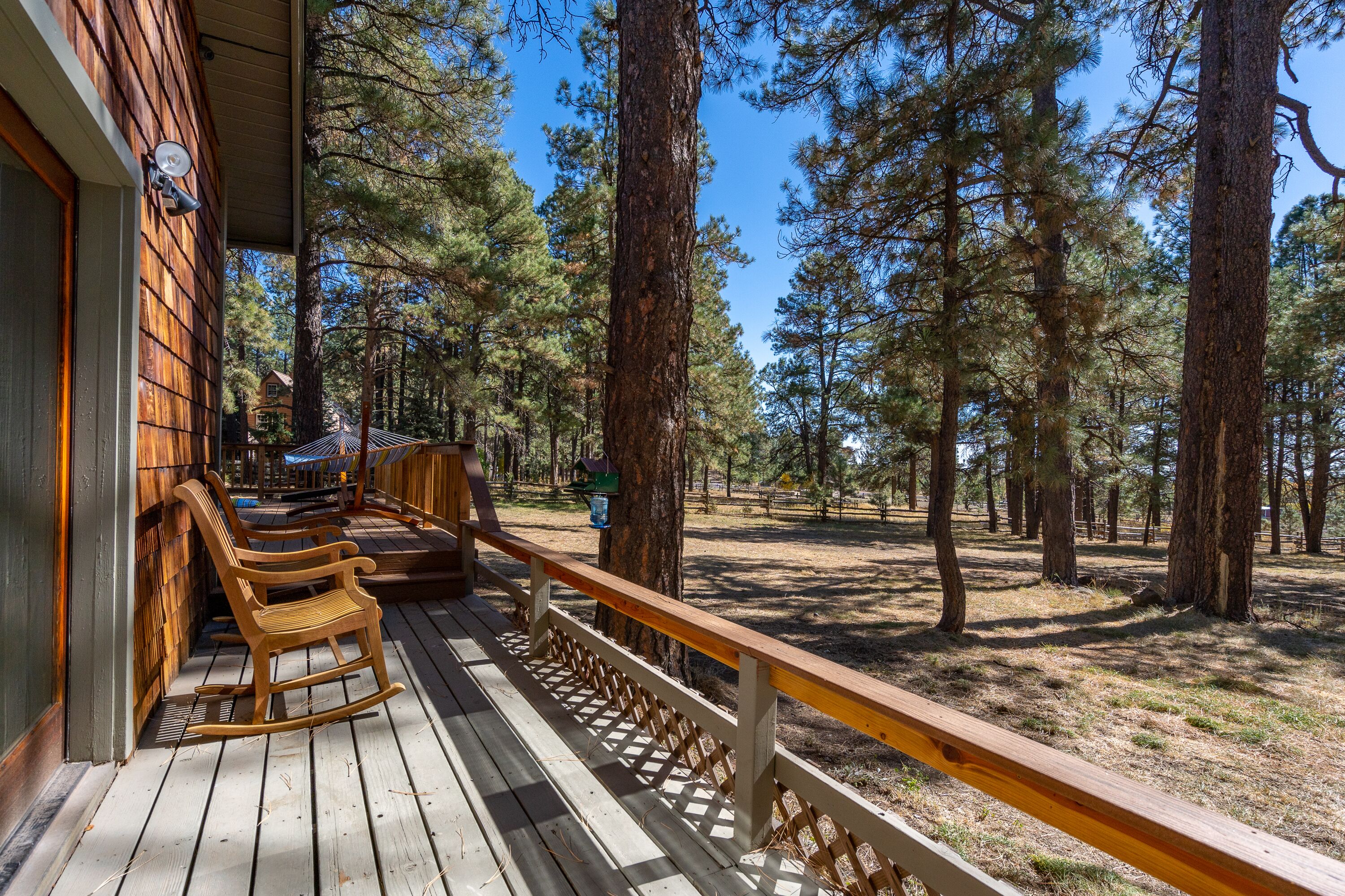 A wooden deck with rocking chairs and a wooden railing overlooking a forested area.