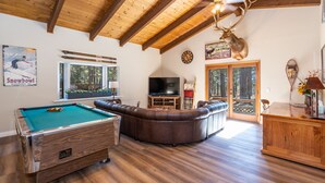 Una sala de estar acogedora con mesa de billar, sofá de cuero y cabeza de venado decorativa.
