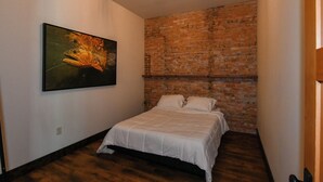 Ein Schlafzimmer mit Backsteinwand, einem Bett mit weißer Bettwäsche und einem Bild von einem Fisch an der Wand.