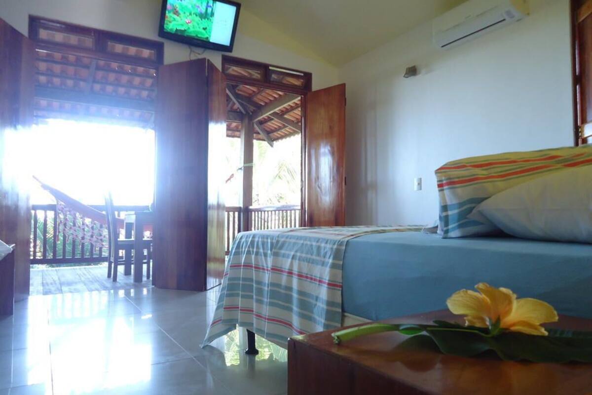 Una habitación con una cama, televisión montada en la pared, una mesa de madera y un balcón con vistas al exterior.
