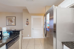 Kitchen features a stainless steel refrigerator, black granite countertop, and a decorative door with a framed artwork above.