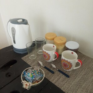 A table with a kettle, two cups, two jars, a spoon, and a small bowl with a packet of snacks. - Boel Boutique 2 (Guayaquil)