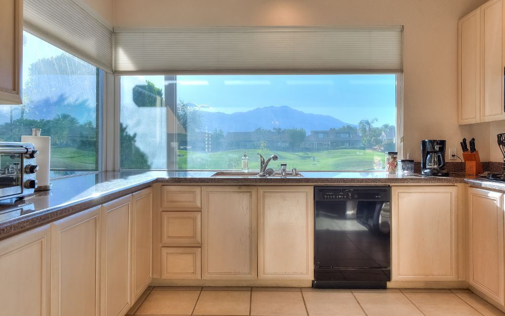 A kitchen with a dishwasher, a coffee maker, and a view of a golf course.